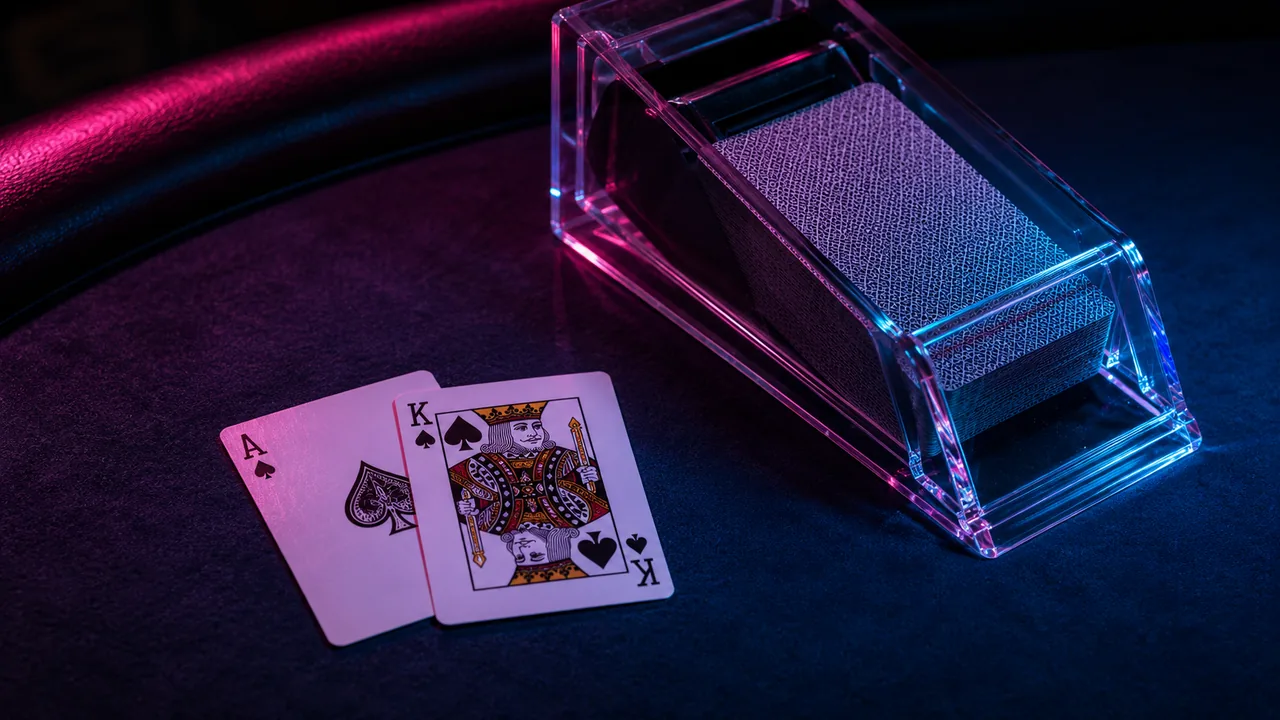 Blackjack cards fanned on a deep-blue casino felt under neon light.
